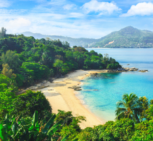 Bucht mit Sandstrand, tropischer Vegetation und türkisfarbenem Wasser auf der Insel Phuket in Thailand, mit bewaldeten Hügeln im Hintergrund.