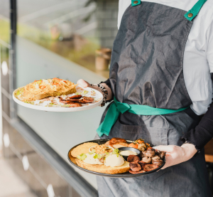 Kellnerin trägt zwei Teller mit modernen Gerichten in einem Café, typisch für Melbournes vielfältige Food-Szene.