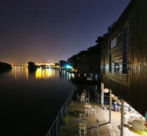 Nächtliche Szene an der Donau mit beleuchteten schwimmenden Bars und Cafés, Lichter spiegeln sich im ruhigen Wasser.