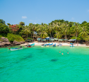 Kleine tropische Bucht in Vietnam mit Booten im klaren gr&uuml;nen Wasser, umgeben von Palmen und dichter Vegetation.