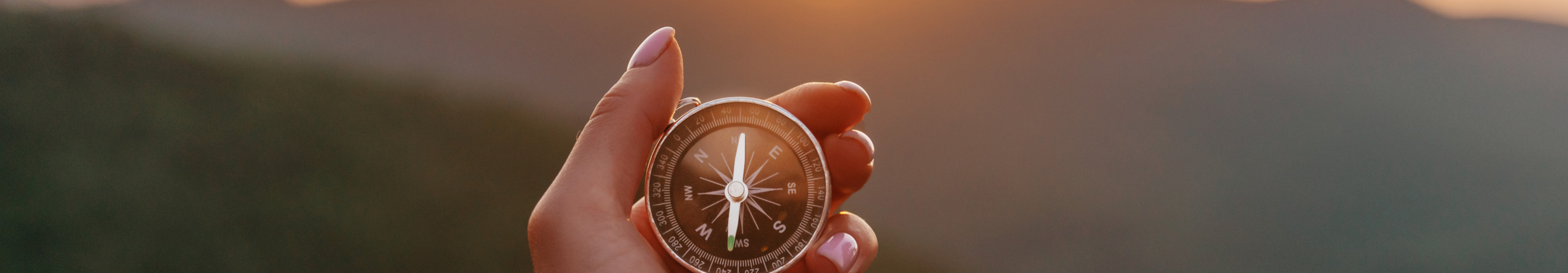 Hand h&auml;lt einen Kompass vor Sonnenuntergang &uuml;ber einer Berglandschaft.