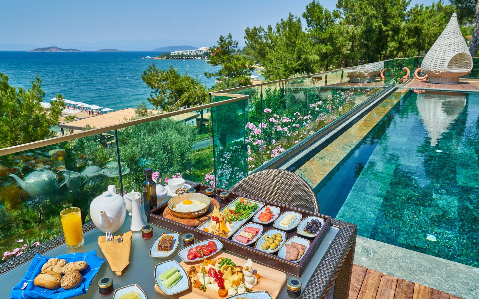 Pauschalurlaub: Gedeckter Tisch mit Fr&uuml;hst&uuml;ck am Pool eines Hotels mit Meerblick