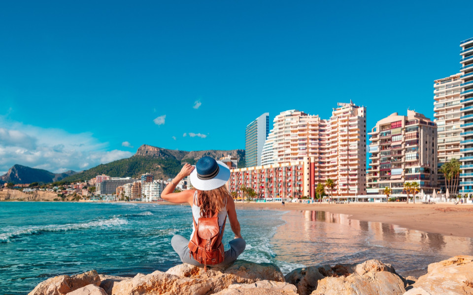 Frau sitzt am Strand mit Stadt im Hintergrund