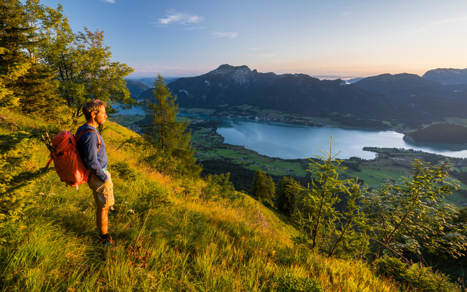 Wanderer steht oberhalb des Wolfgangsees im Salzkammergut mit Blick auf See, Tal und Berge.