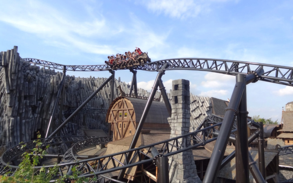 Achterbahn im Phantasialand, mit Fahrgästen, die über eine kurvige Strecke nahe einem thematisierten Gebäude fahren.