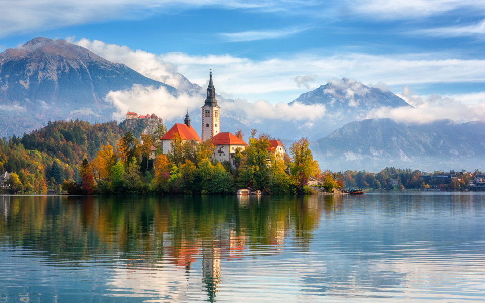 Berühmter Bleder See in Slowenien, atemberaubende Herbstlandschaft. Malerischer Blick auf den See, Insel mit Kirche, Burg Bled, Berge und blauer Himmel mit Wolken,