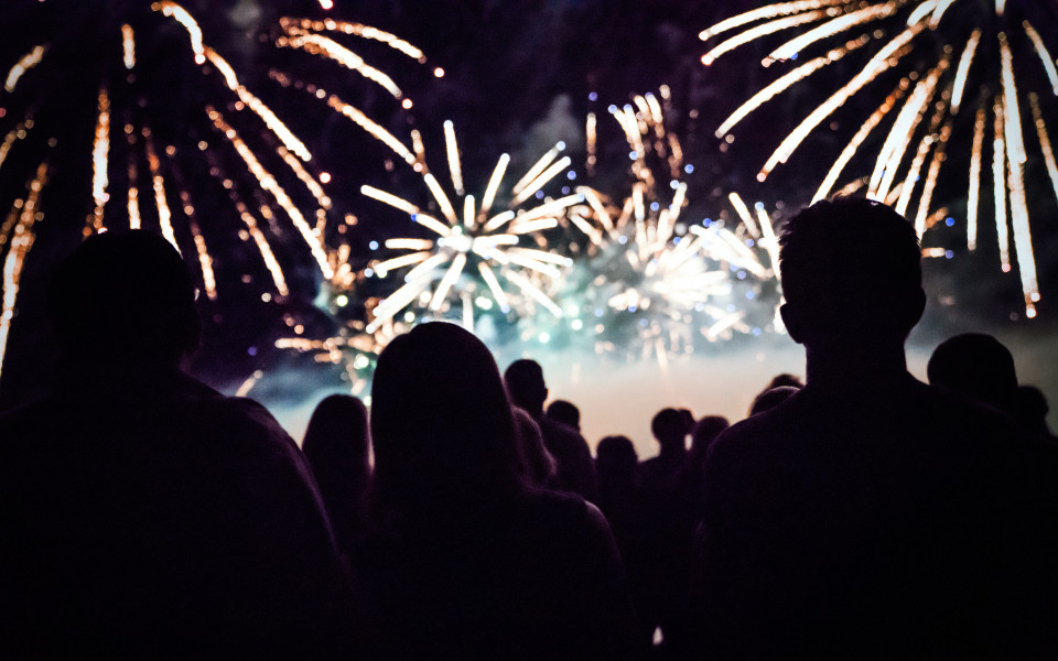 Menschen schauen in der Silvesternacht auf ein farbenfrohes Feuerwerk am Himmel – festliche Stimmung zum Jahreswechsel.